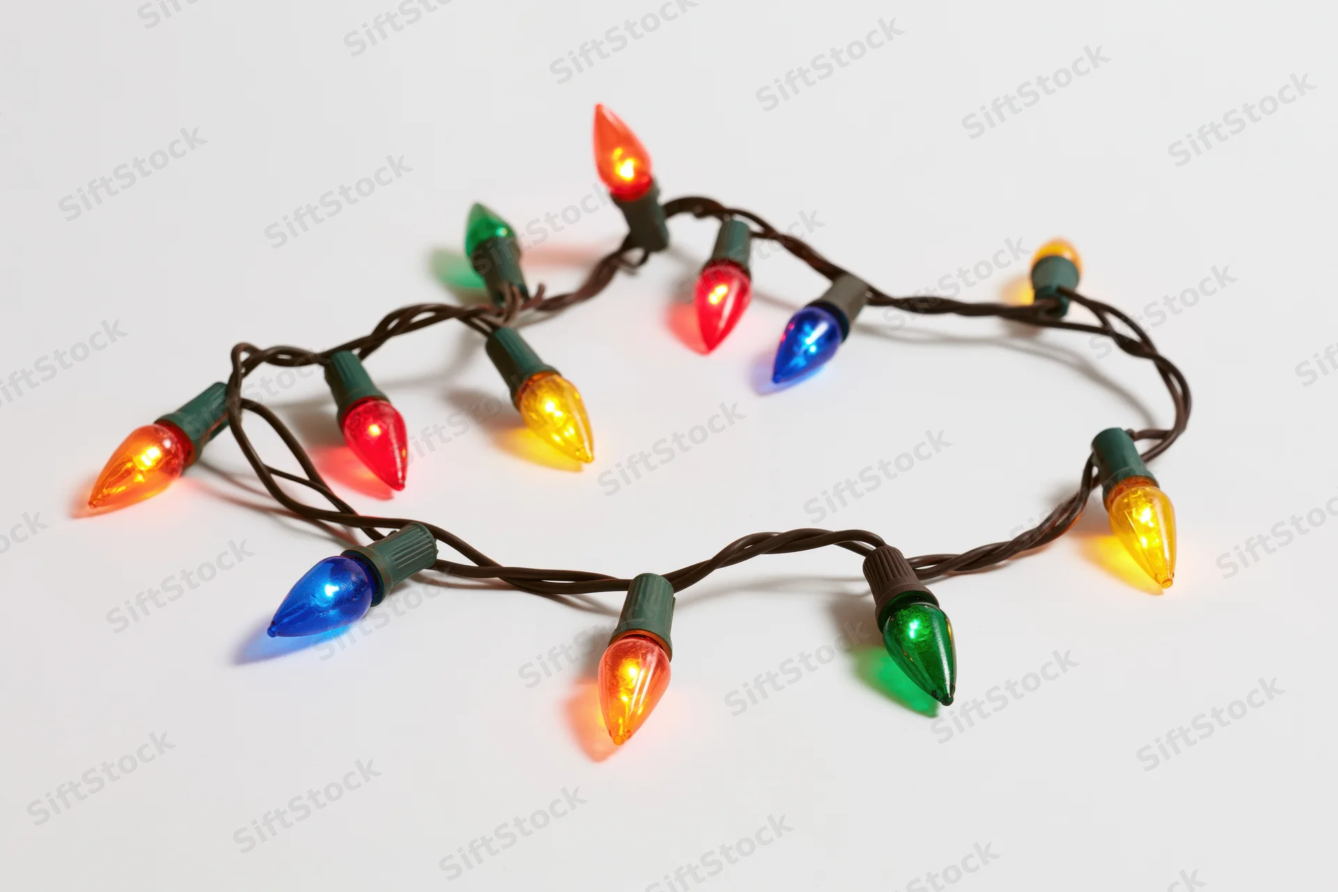 A single strand of multicolored christmas lights arranged in a loose loop on a white background