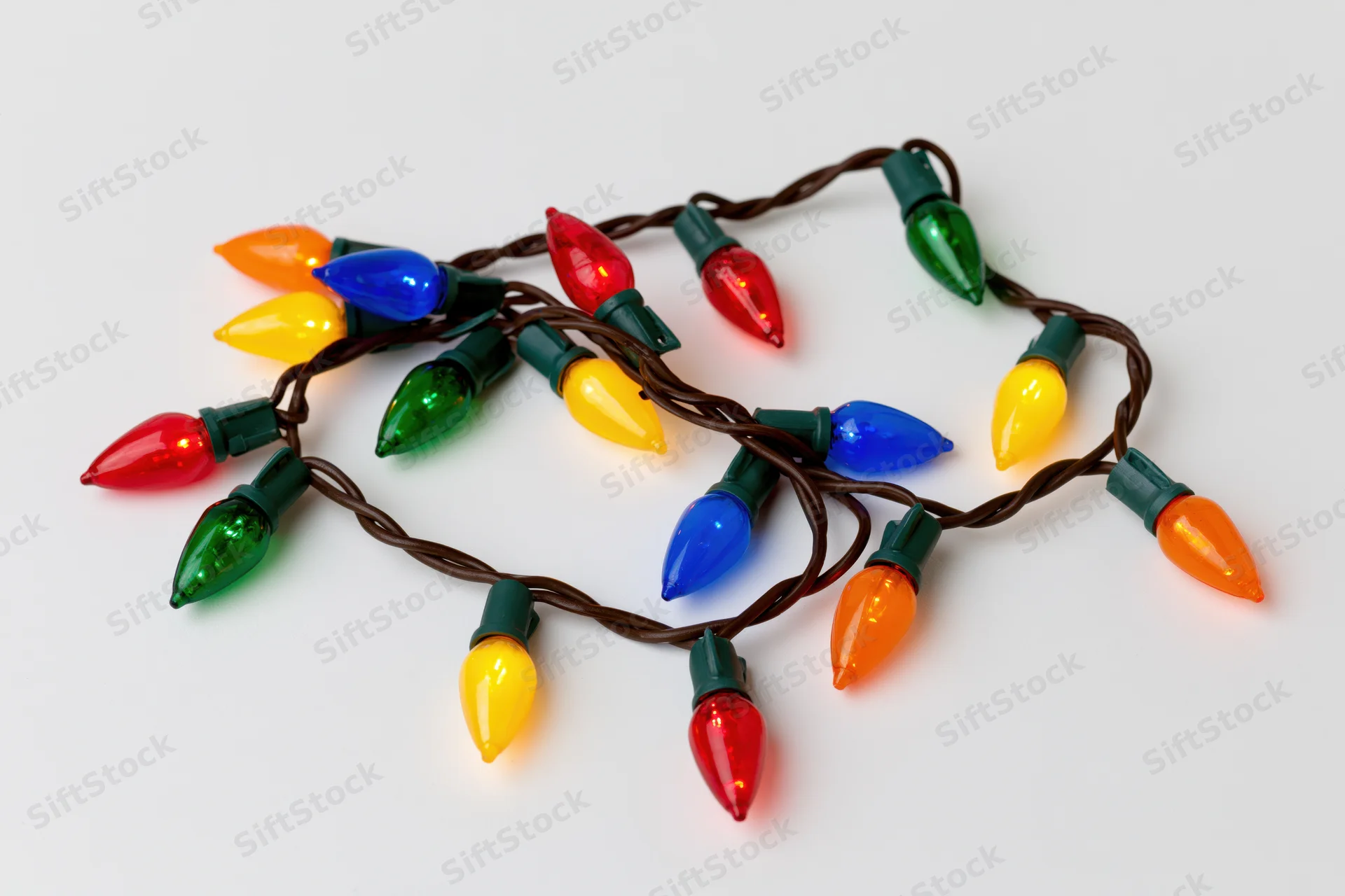 A single strand of multicolored christmas lights arranged in a loose coil on a white surface