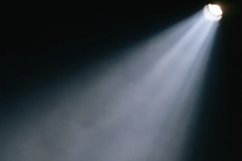 Single spotlight beam cutting diagonally through smoke in a dark theater space