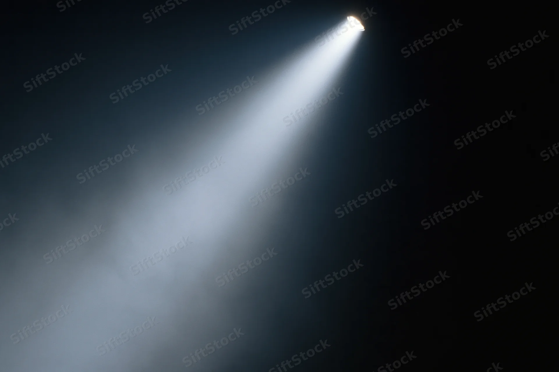 Single spotlight beam cutting diagonally through dark smoky air on stage