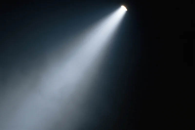 Single spotlight beam cutting diagonally through dark smoky air on stage