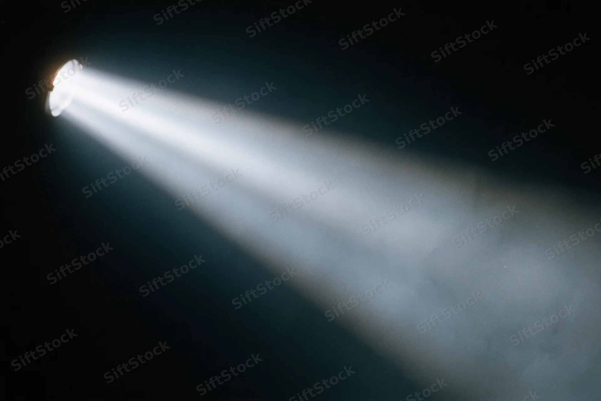 Single spotlight beam cutting diagonally through dark smoky air on stage