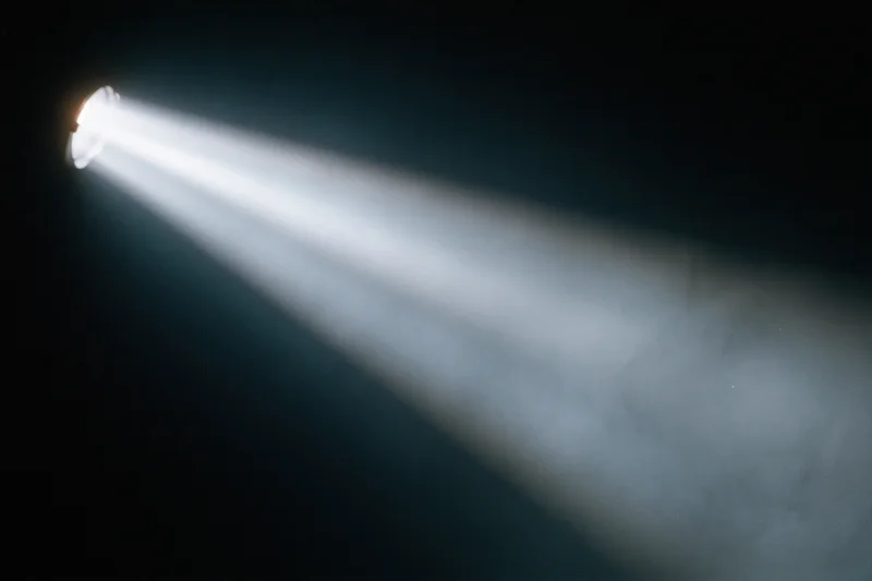 Single spotlight beam cutting diagonally through dark smoky air on stage