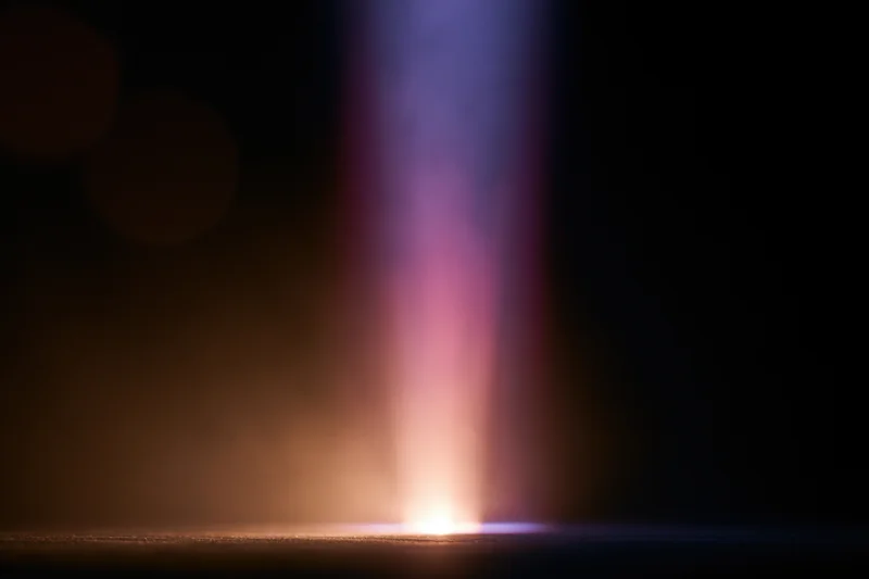 Vertical beam of light rising from a bright point on dark background with color gradient and soft haze