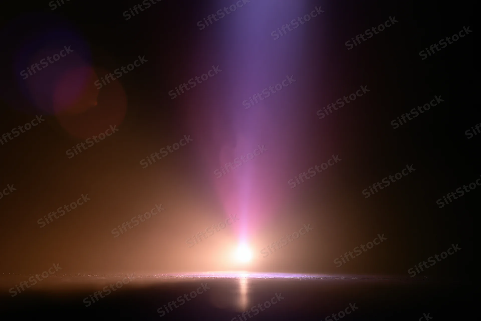 Vertical beam of light rising from a bright point on a dark reflective surface