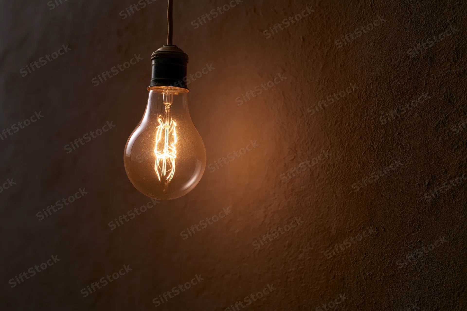 Vintage incandescent lightbulb hanging from ceiling against dark textured wall with warm glow