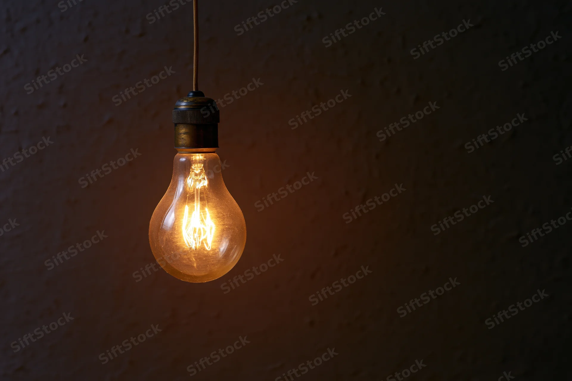 Vintage incandescent lightbulb hanging from a thin wire against a dark textured wall