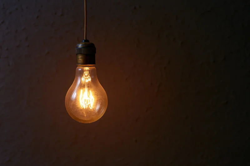 Vintage incandescent lightbulb hanging from a thin wire against a dark textured wall