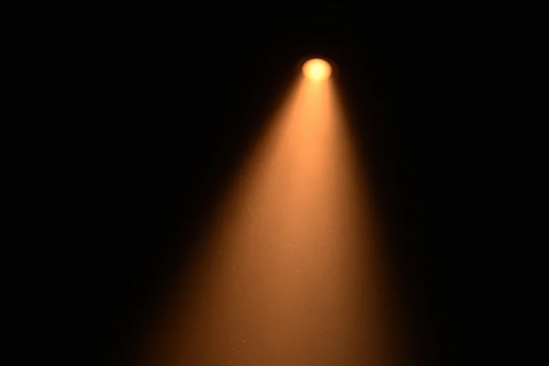 Warm amber spotlight beam cutting downward through dark space