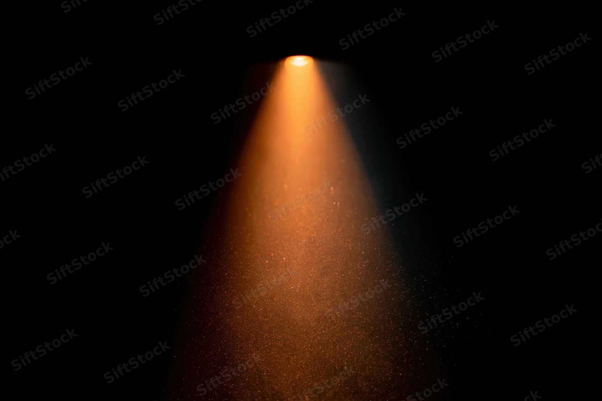 Warm amber spotlight beam cutting through dust particles in dark space