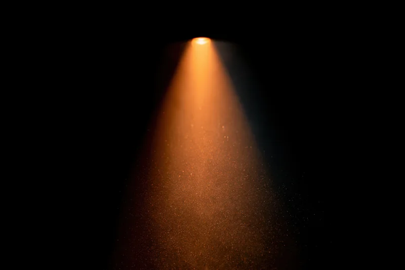 Warm amber spotlight beam cutting through dust particles in dark space