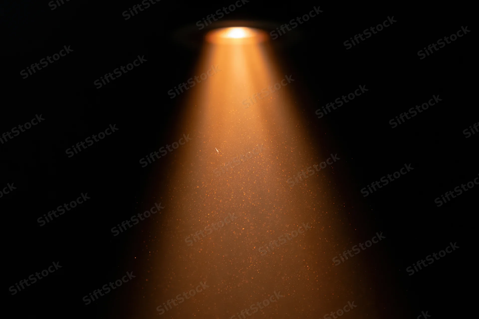 Warm amber spotlight beam cutting downward through floating dust particles in dark space