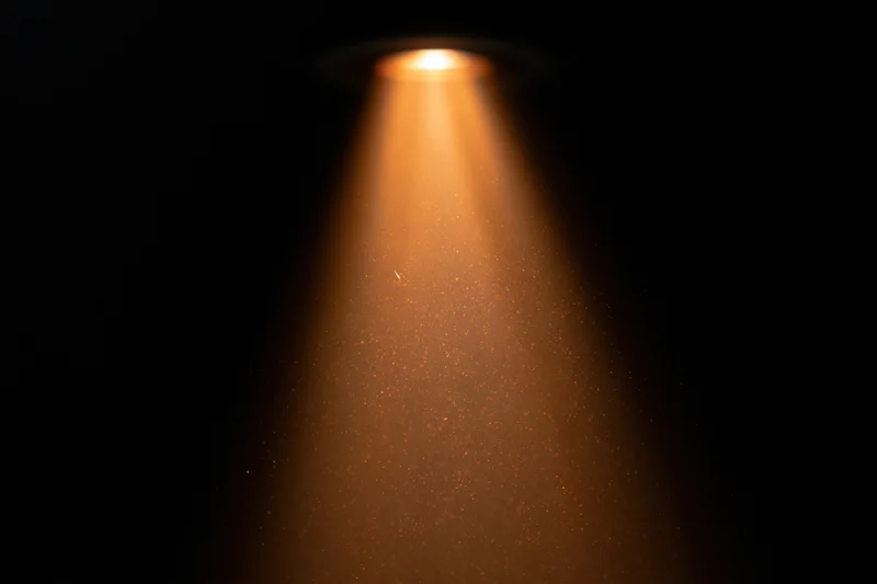 Warm amber spotlight beam cutting downward through floating dust particles in dark space
