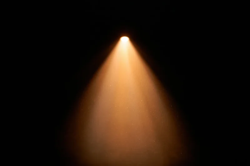 Warm amber spotlight beam cutting downward through dark space