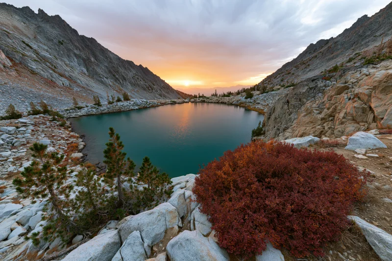Turquoise alpine lake nestled in rocky mountain valley at sunset with autumn foliage and pine trees surrounding it
