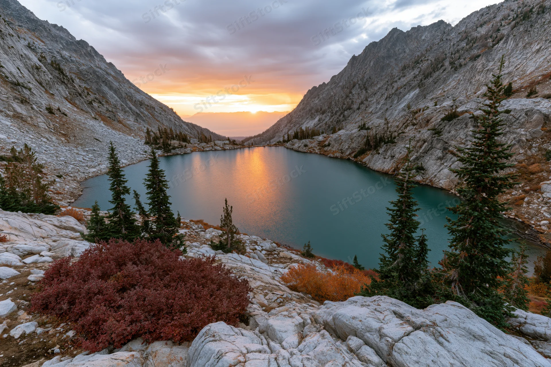 Turquoise alpine lake reflecting sunset light in a rocky mountain valley surrounded by pine trees and autumn foliage