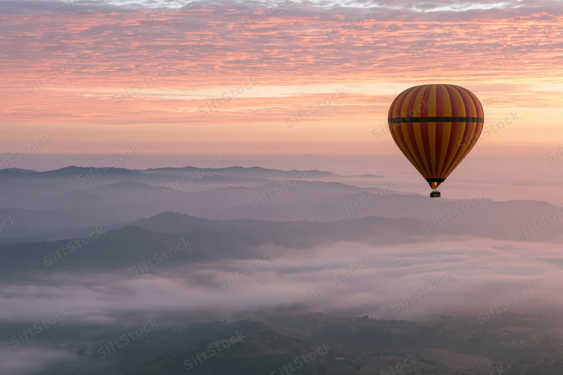 Striped yellow red and black hot air balloon floating above misty mountains at sunrise