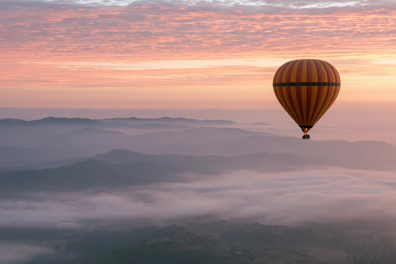 Striped yellow red and black hot air balloon floating above misty mountains at sunrise