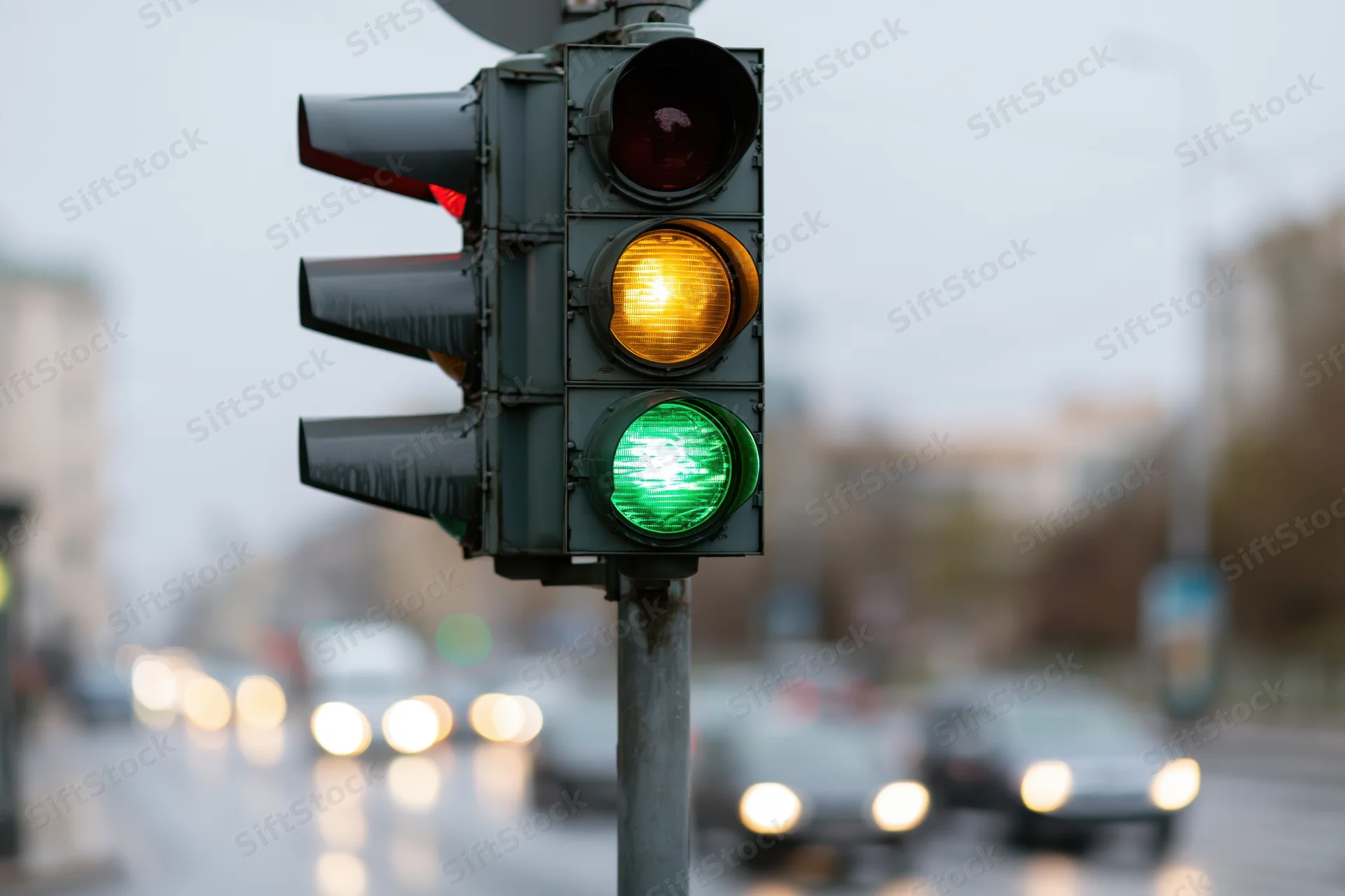 Traffic light showing green and yellow signals on a wet city street with blurred vehicles in the background