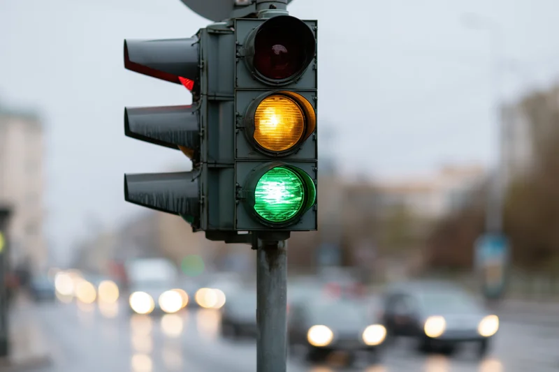 Traffic light showing green and yellow signals on a wet city street with blurred vehicles in the background