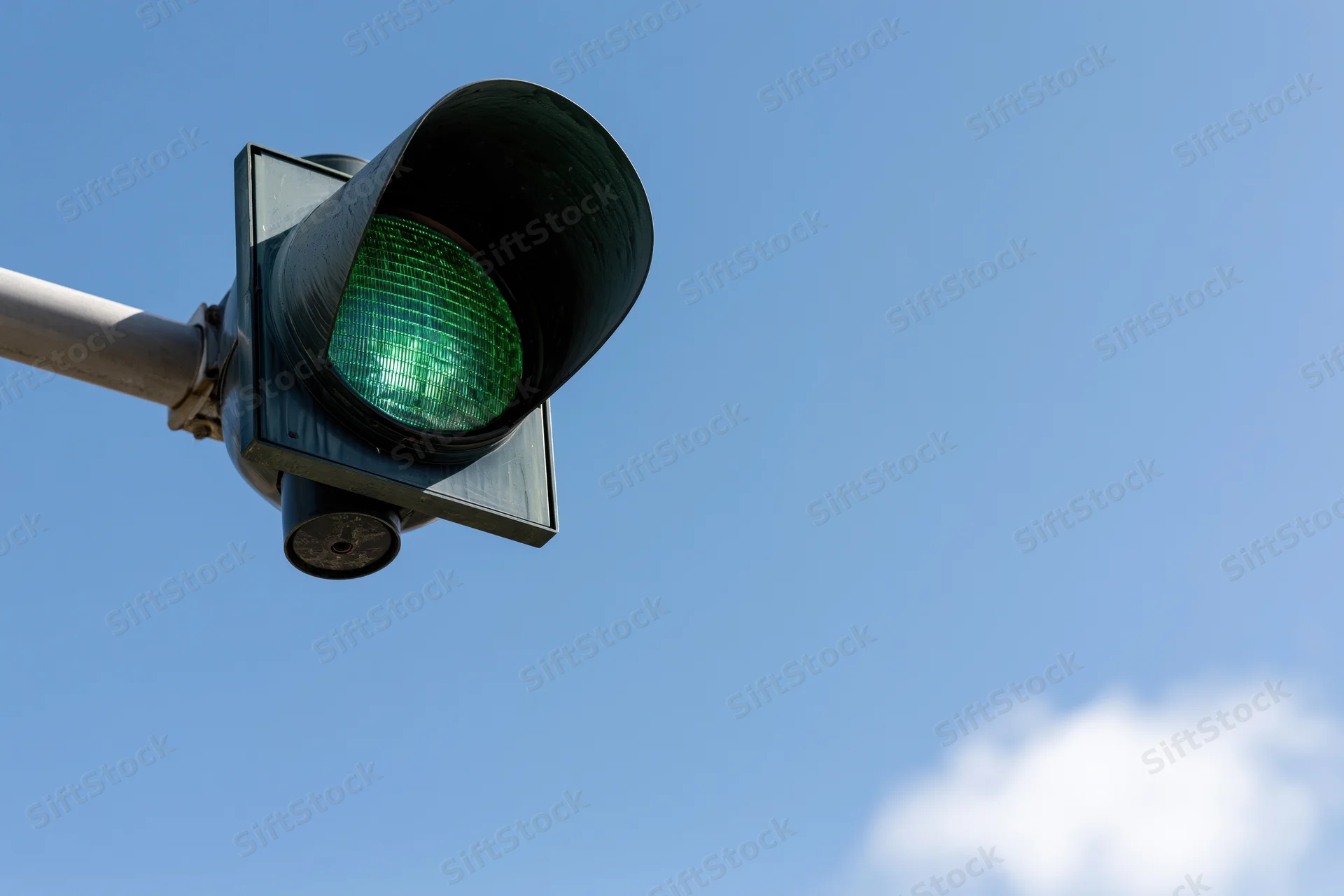 Green traffic light mounted on metal arm against blue sky