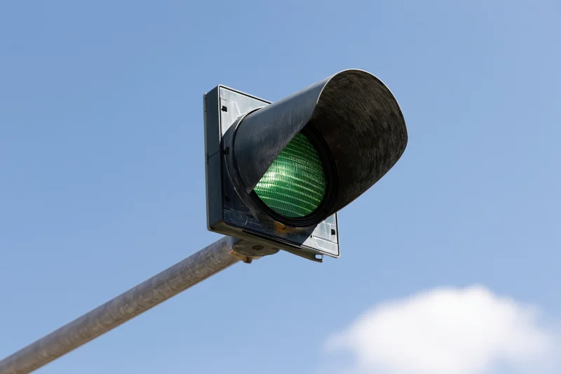 Green traffic light mounted on metal arm against blue sky