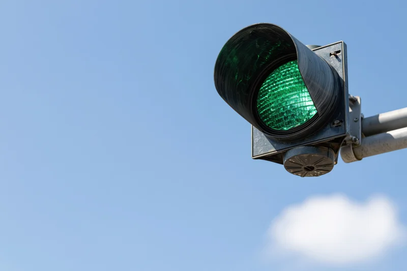 Green traffic light mounted on metal arm against blue sky
