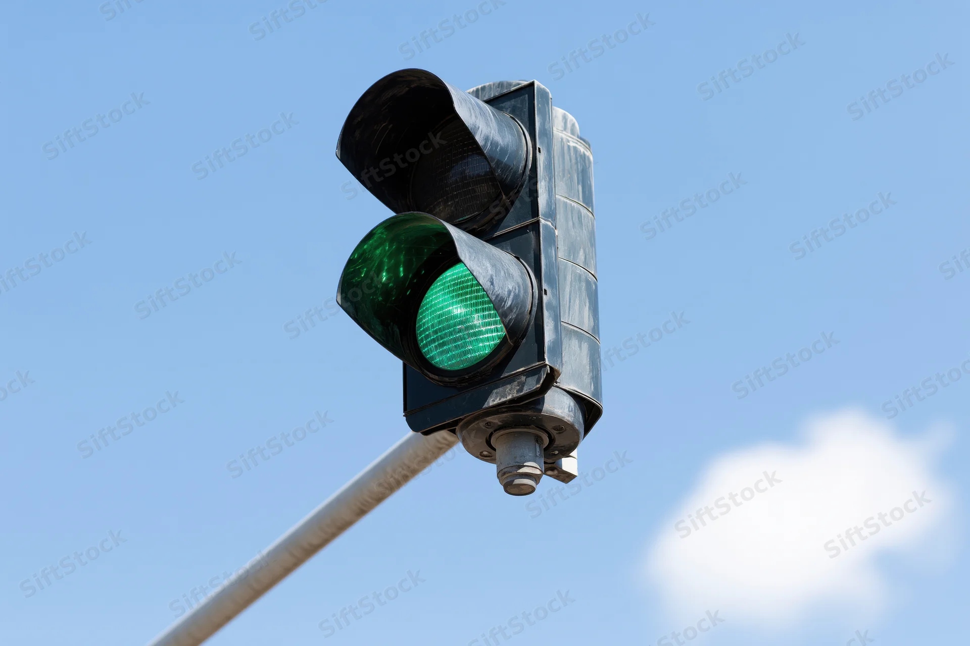 Green traffic light mounted on metal arm against blue sky