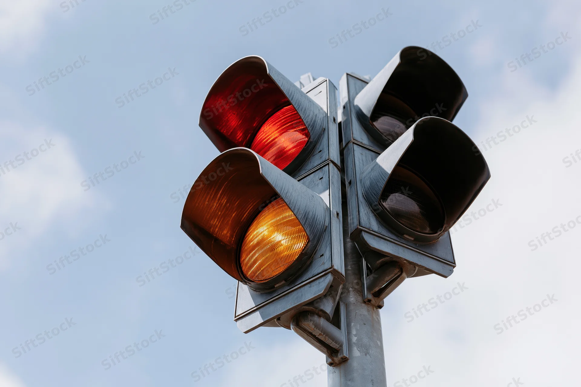 Traffic light with red and amber signals illuminated against a cloudy sky