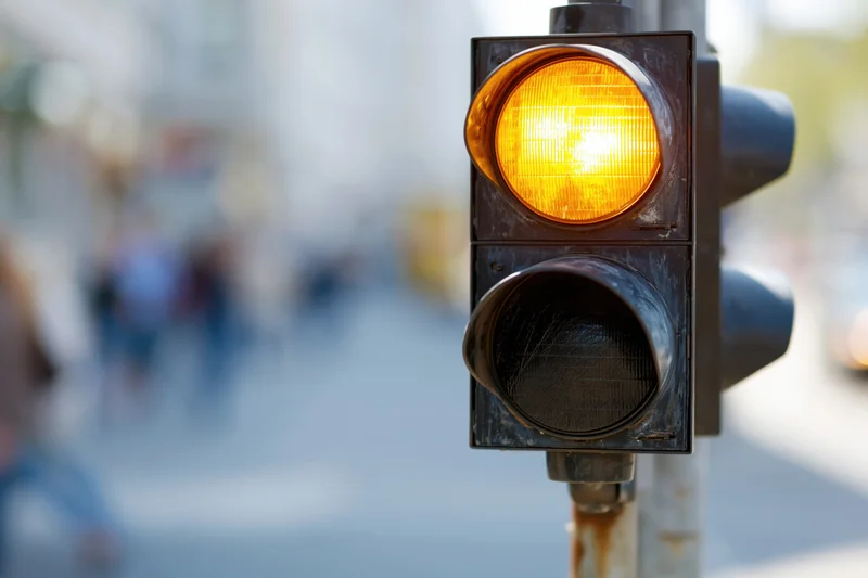 Vertical traffic light with amber signal illuminated on metal pole in urban street setting