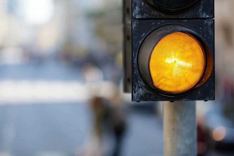 Vertical traffic light with amber signal illuminated on metal pole in urban street setting