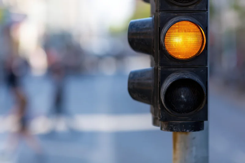 Vertical traffic light showing amber signal mounted on metal pole in urban street setting