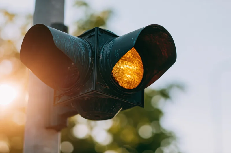 Weathered black metal traffic light with amber signal illuminated on a city street during daytime
