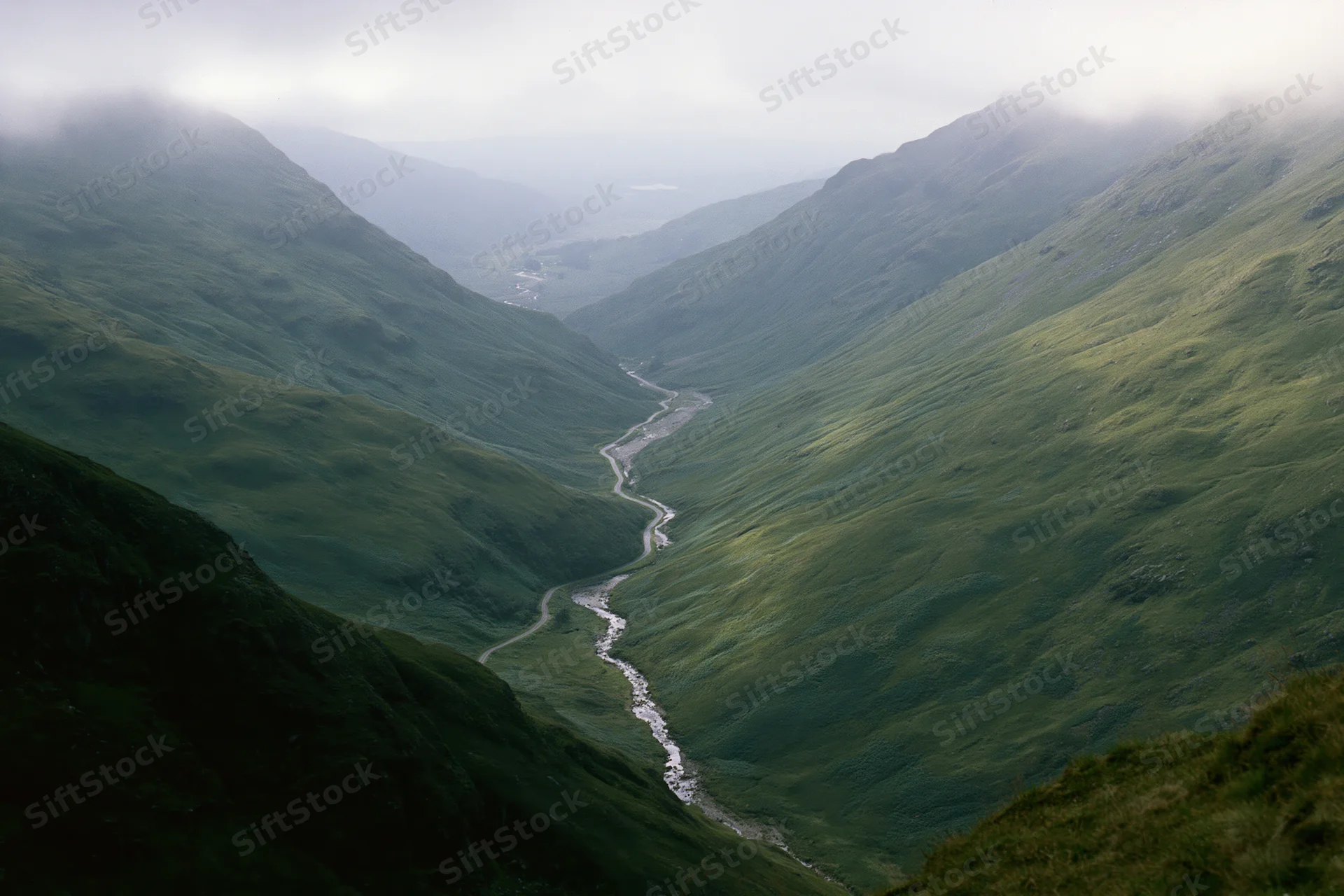 Winding single-track road and narrow stream running through a green mountain valley in the Scottish Highlands