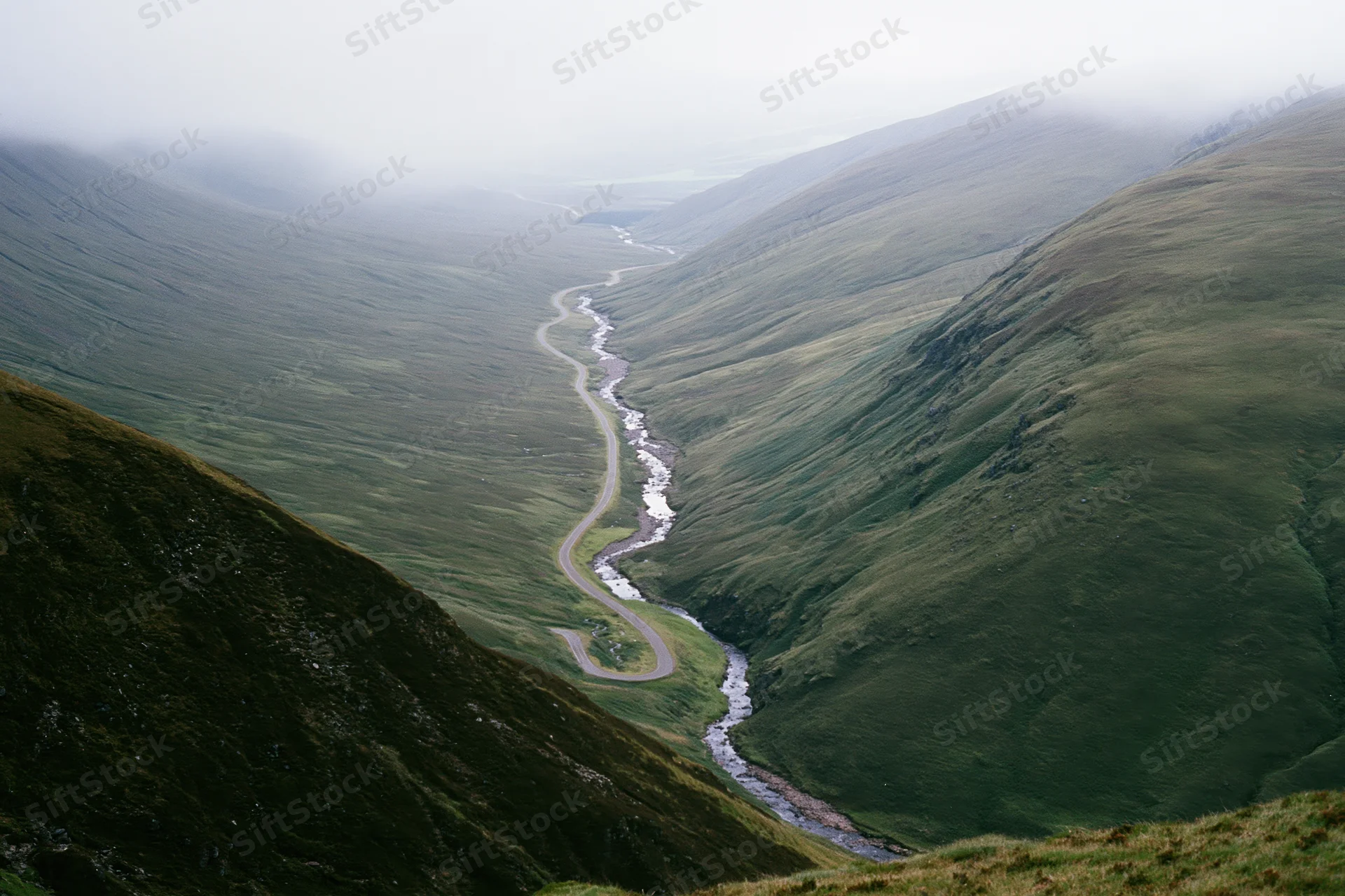 Winding single-track road and narrow stream running parallel through a green mountain valley
