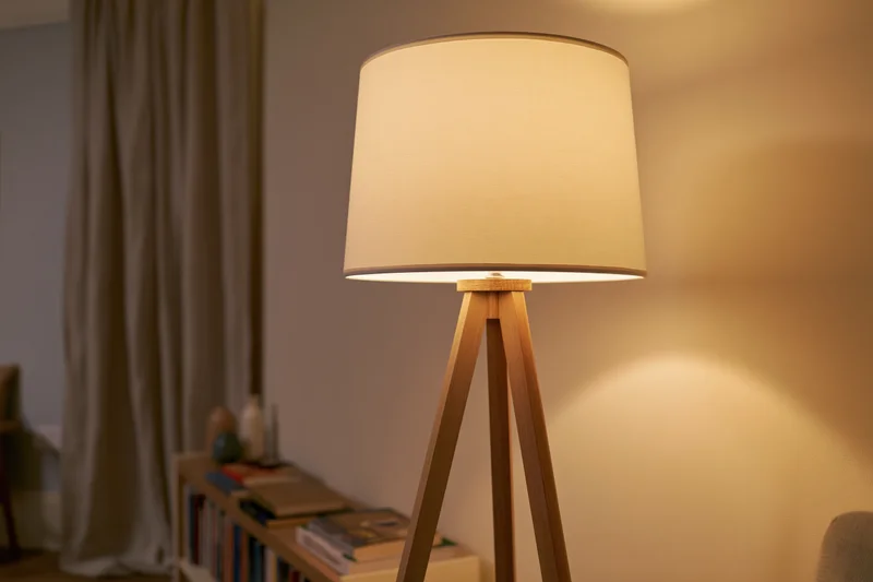 Wooden tripod floor lamp with white drum shade glowing warmly in a living room interior