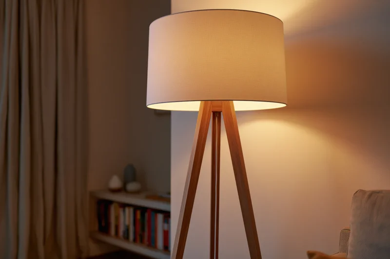 Wooden tripod floor lamp with white drum shade glowing warmly in a living room corner