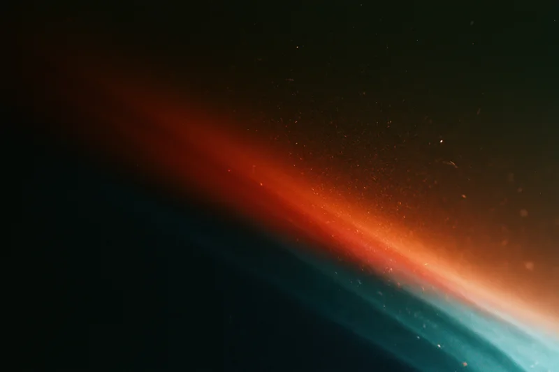 Diagonal analog film light leak across dark background with red orange blue gradient and dust particles