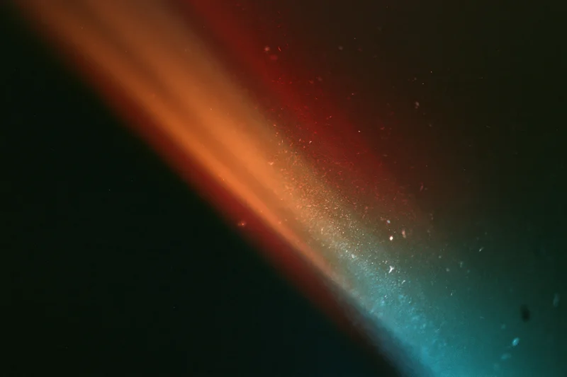 Diagonal analog film light leak across dark background with red orange and teal gradient