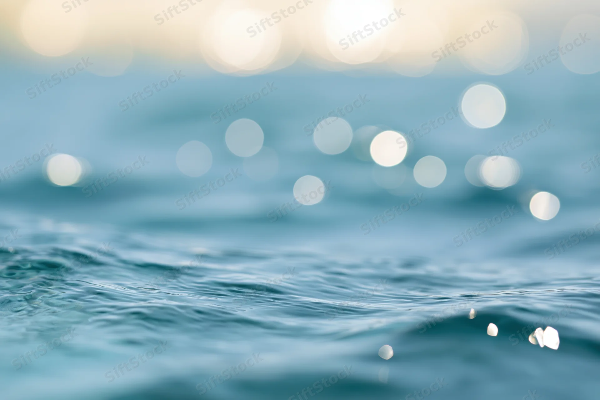 Sunlit ocean water surface with bokeh light reflections and gentle ripples