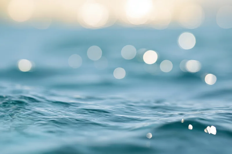 Sunlit ocean water surface with bokeh light reflections and gentle ripples