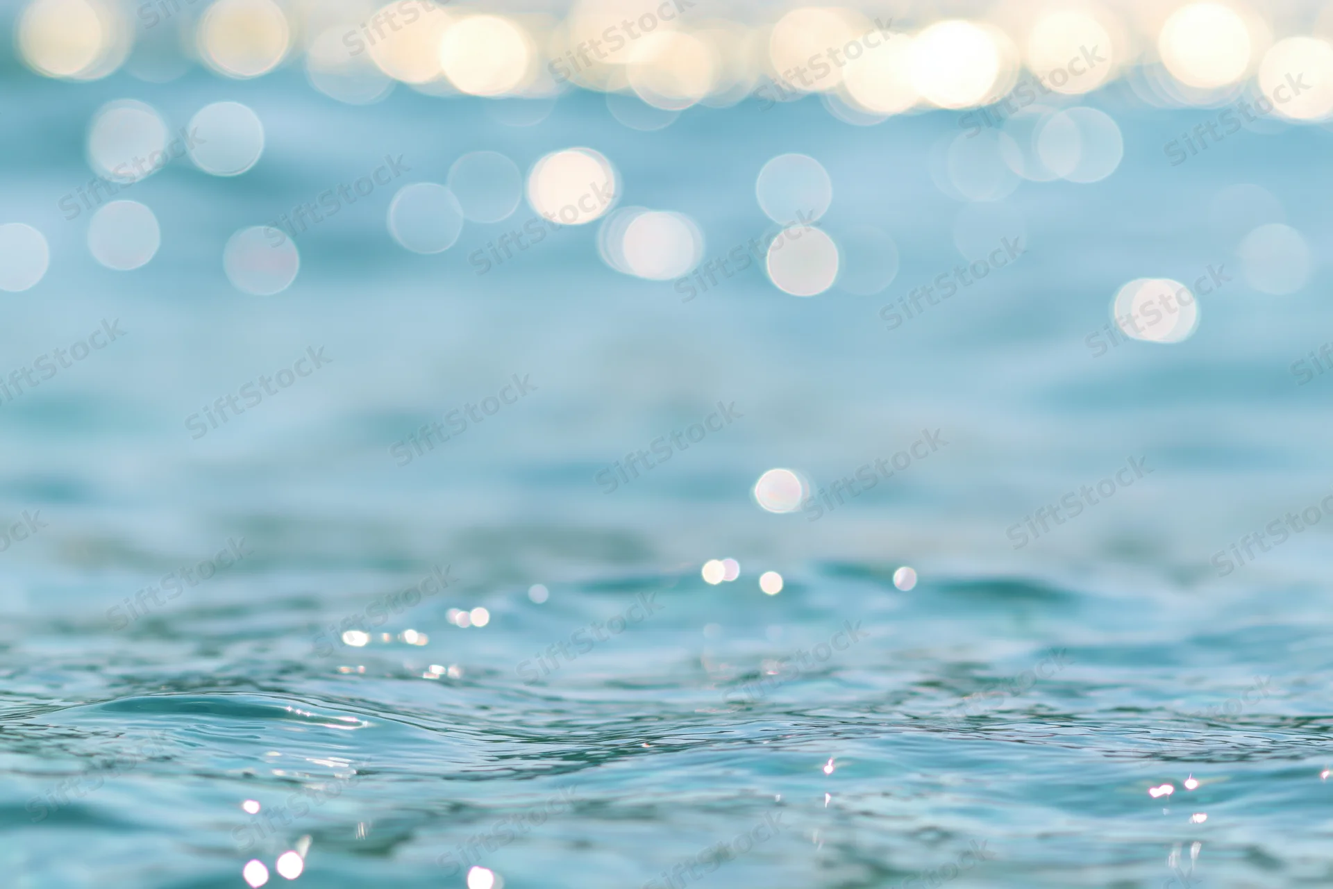 Sunlit ocean surface with shimmering ripples and bokeh reflections in the background
