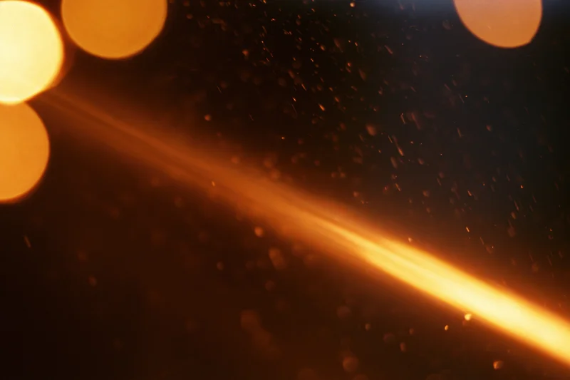 Warm amber light leaking across dark space with floating particles and bokeh highlights