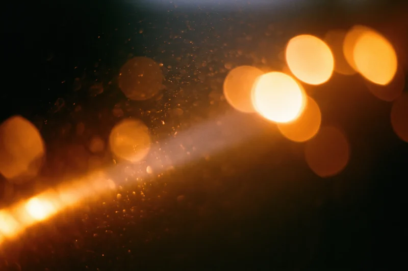 Warm amber light leaking across a dark surface with bokeh and floating particles
