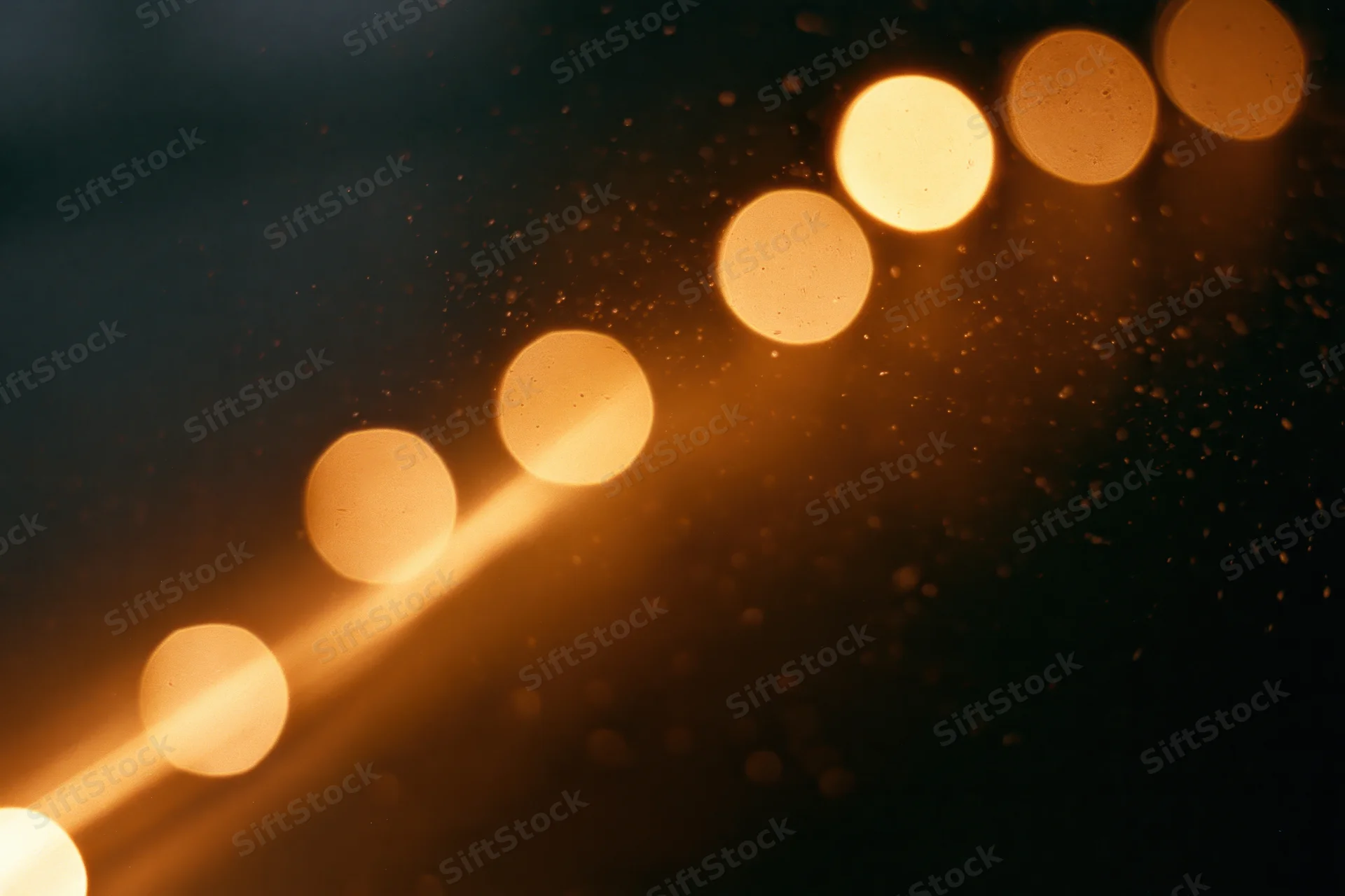 Warm amber bokeh lights glowing softly in dark space with visible dust particles and lens flare