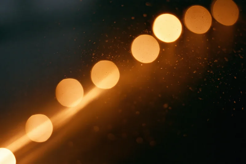 Warm amber bokeh lights glowing softly in dark space with visible dust particles and lens flare