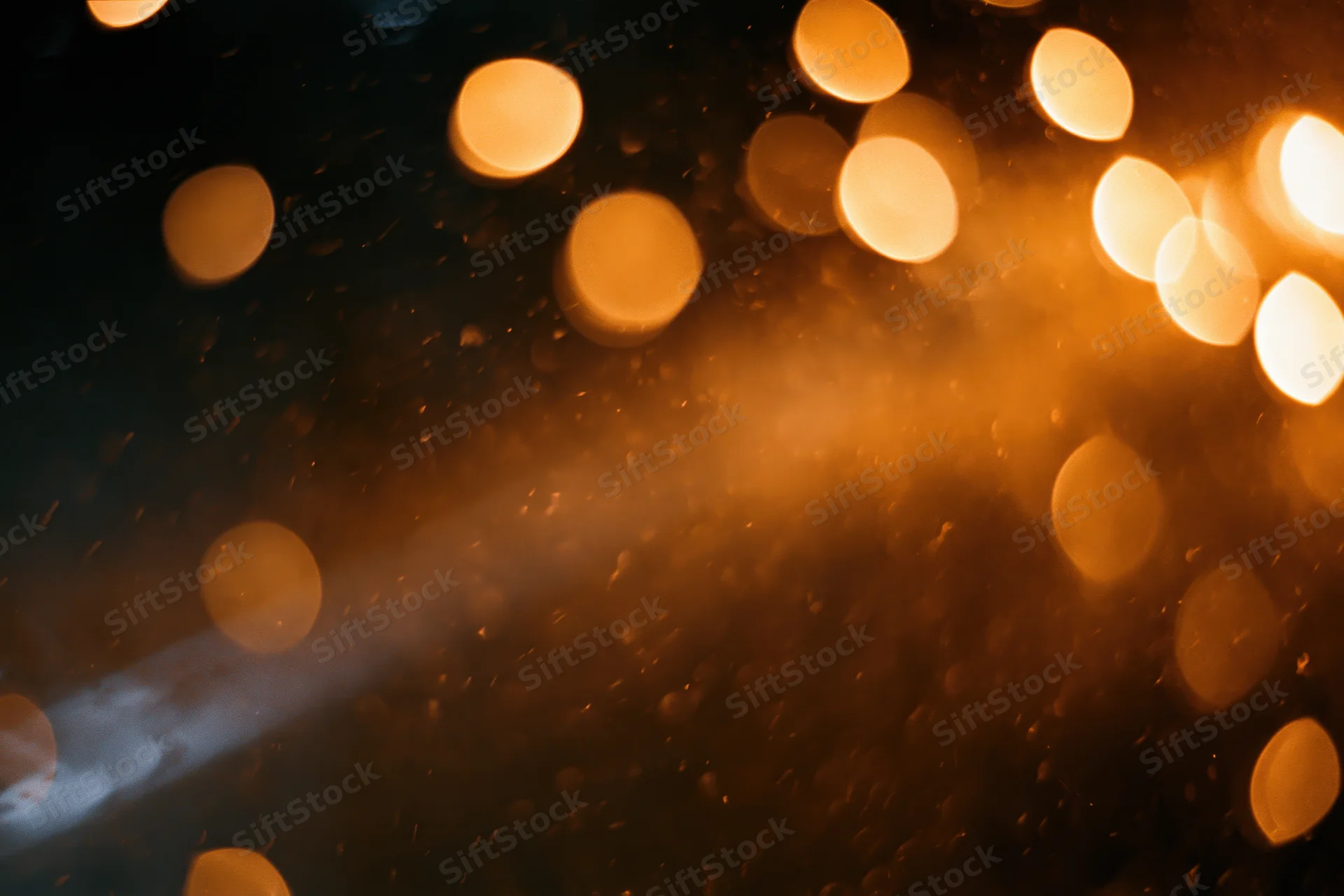 Warm amber bokeh lights glowing softly across a dark wet surface with rain droplets
