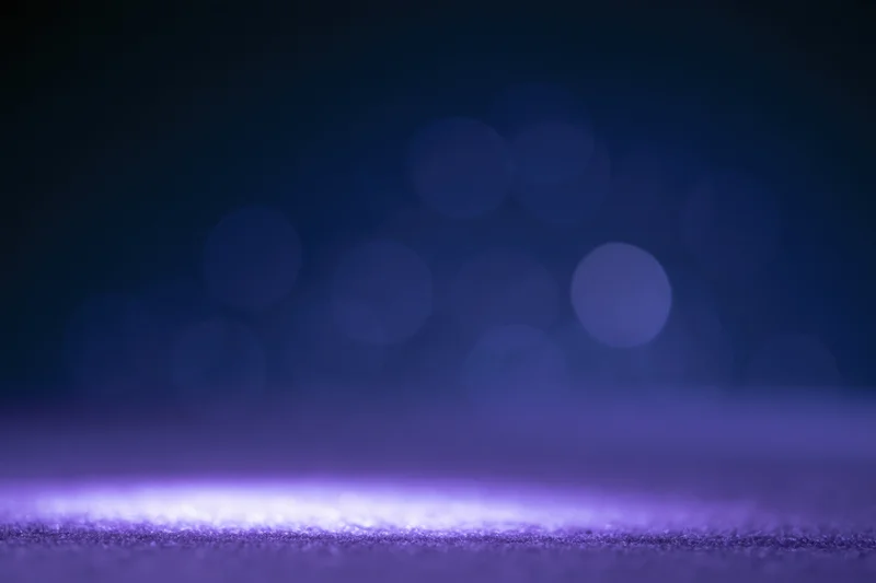 Abstract dark studio backdrop with soft out-of-focus bokeh lights and glowing purple surface