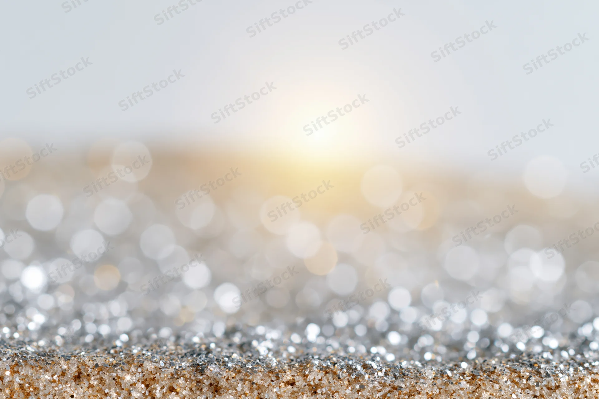 Scattered silver and gold glitter on a surface with blurred bokeh lights in the background