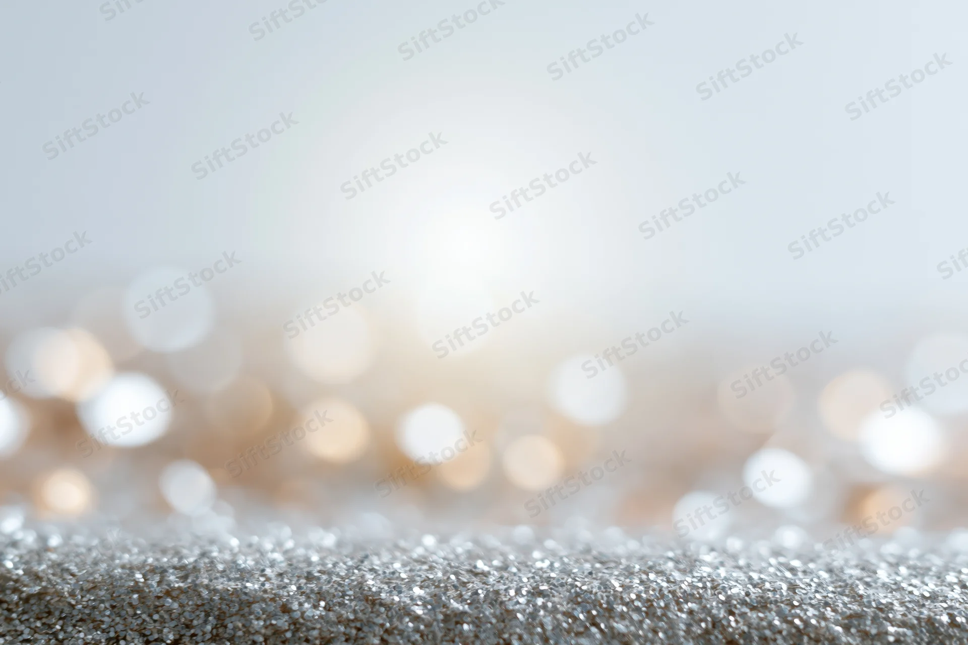 Silver glitter surface with blurred warm bokeh lights in background